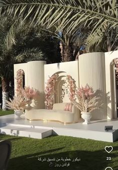 an outdoor seating area with pink flowers and greenery on the grass, surrounded by palm trees