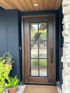 the front door to a home with potted plants on the porch and glass doors