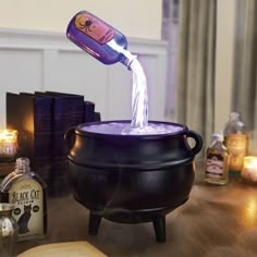 a bottle is pouring into a caulder on a table with books and candles