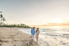 a man and woman walking on the beach at sunset with palm trees in the background