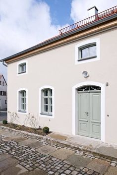 a white house with green doors and windows on cobblestone street in front of it