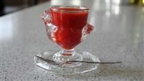 a glass cup filled with red liquid sitting on top of a counter next to a spoon