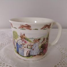 a coffee cup with rabbits on it is sitting on a doily covered tablecloth