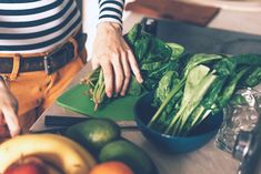 a woman cutting up vegetables on top of a green cutting board next to other fruits and vegetables