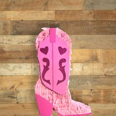 a pair of pink cowboy boots with hearts on the inside and bottom, sitting against a wooden wall