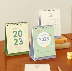 three calendars sitting on top of a wooden table next to books and pencils