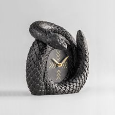 a black and gold clock with two snakes on it's sides, sitting in front of a white background