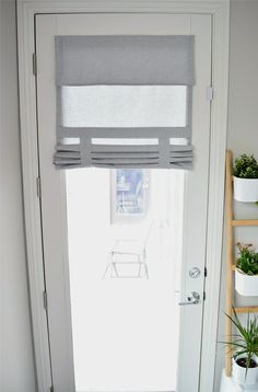 a white door with a gray and white roman blind on the window sill next to a potted plant