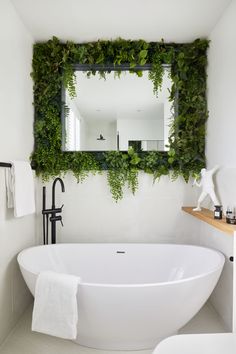 a white bath tub sitting next to a mirror covered in green plants on the wall