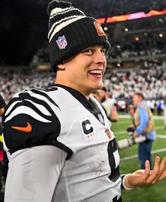 a man in a football uniform standing on the sidelines with his hands out and smiling