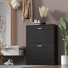 a black dresser sitting next to a mirror and potted plant