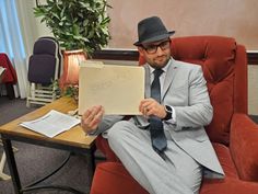 a man in a suit and tie sitting on a chair holding up a piece of paper