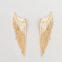 Fringe appliques are accessories that will transform a simple earring into a new, eye-catching, and unparalleled proposition. Once attached behind the ear, this piece will provide movement and charm to the chosen earring.This time, the featured fringe boasts a noble metal structure, gold plated or white rhodium plated, made of gradient-sized chains with an ultra-fine thickness and an ear cuff design.Note: EARRINGS ARE NOT INCLUDED WITH THE ORIGINAL PIECE, IT IS MERELY AN ILLUSTRATION. Gold Metal Ear Climbers For Pierced Ears, Gold Metal Pierced Ear Climbers, Elegant Gold Metal Ear Climbers, Gold Metal Fringe Tassel Earrings, Gold Fringe Earrings In Brass, Gold Metal Tassel Earrings With Fringe, Gold Fringe Metal Chandelier Earrings, Gold Fringe Chandelier Earrings, Gold Single Ear Cuff