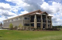 a large house sitting on top of a lush green field under a blue sky with clouds