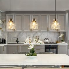 a kitchen with marble counter tops and gold accents on the cabinets, along with white flowers in a vase