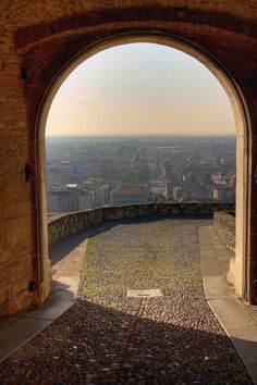 an arch in the side of a brick building with a view of a city below