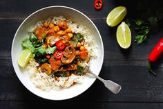 a white bowl filled with rice and vegetables next to sliced limes on a wooden table