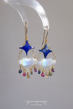 ---- Welcome to CiaoQiao Shop ----- These enchanting earrings feature beautifully crafted blue star gemstones paired with iridescent cloud-shaped moonstones, creating a dreamy and whimsical design. Dangling from delicate gold chains, a selection of colorful gemstones adds a touch of sparkle and elegance, reminiscent of twinkling stars in the night sky. Perfect for adding a celestial touch to your outfit, these handcrafted earrings are ideal for both special occasions and everyday wear. They make a thoughtful and unique gift for anyone who loves the beauty of the cosmos. Please note: natural stones will have flaws and no two stones will look exactly alike. Tips for making your Jewelry last longer - Remove your jewelry before you swim in chlorine or salt water. - Remove your jewelry before p Celestial Iridescent Earrings For Gift, Unique Rainbow Drop Earrings, Whimsical Rainbow Dangle Jewelry, Celestial Gemstone Drop Earrings, Celestial Moonstone Earrings, Nickel-free Celestial Moonstone Earrings, Celestial Blue Pierced Earrings, Blue Celestial Pierced Earrings, Blue Gemstone Chandelier Earrings For Gifts