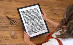 a woman holding up a framed book with writing on it and some scissors next to it