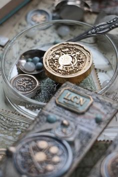 an assortment of buttons and other items on a glass plate with metal spoons next to it