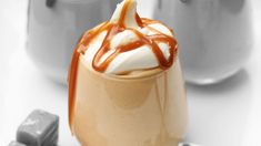 there is a dessert with caramel and whipped cream on top in a glass cup