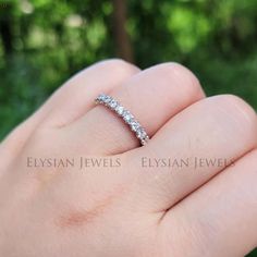 a woman's hand with a diamond ring on her finger in front of some trees