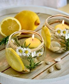 two lemons and some white flowers are in small glass bowls with water on a wooden table