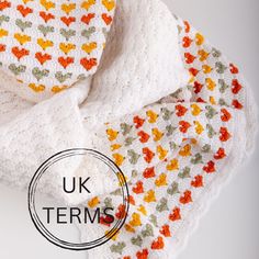 a crocheted blanket with an orange and yellow flower on it, next to a white knitted scarf