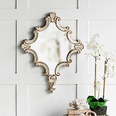 an ornate mirror on the wall above a table with books and flowers in front of it