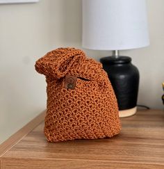 a crocheted bag sitting on top of a wooden table next to a lamp