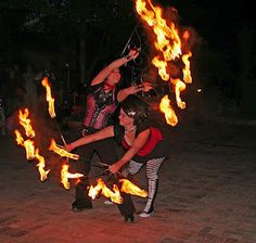 two people are performing with fire sticks in the middle of a brick floored area