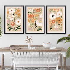 three framed paintings on the wall above a dining room table with white chairs and a wooden bench