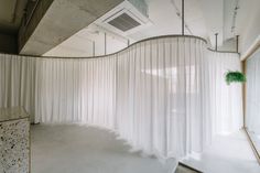 an empty room with white drapes hanging from the ceiling and a green plant in the corner