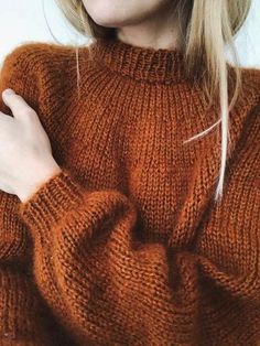 a woman with blonde hair wearing a brown sweater and holding her hands on her chest