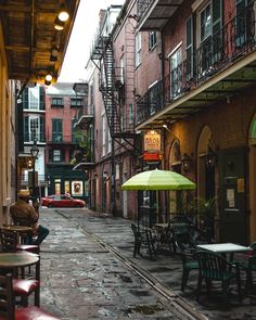 an alleyway with tables and chairs on the side walk, surrounded by brick buildings