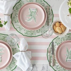 pink and green place setting with plates, silverware, napkins and flowers on striped tablecloth