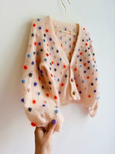 a hand is holding up a sweater hanging on a clothesline with colorful dots all over it