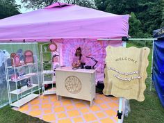 a woman is standing behind a pink and white tent with an ice cream stand in front of it