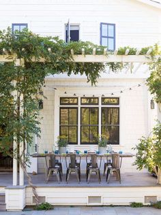 an outdoor dining table and chairs on a patio with trees in front of the house