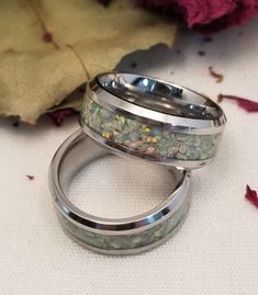 two wedding rings sitting on top of each other next to a leaf and flower petals