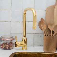 kitchen utensils and wooden spoons are sitting on the counter next to a gold faucet