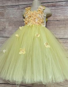 This adorable and beautiful dress is hand-made by Stella with full of love and affection and is perfect for your lovely girl for her birthday, being a flower girl, for the wedding party, being bridesmaid, for the christening, or any other special occasion. The dress features 6-inch-long soft crochet which is completely covered with beautiful yellow flowers that are scattered over the skirt and extending onto the shoulder straps. The matching satin shoulder straps are adjustable and tie into a bo Cute Sleeveless Fairy Dress For Wedding, Cute Sleeveless Tutu Dress For Wedding, Yellow Sleeveless Tutu Dress For Wedding, Whimsical Summer Tutu Dress For First Birthday, Birthday Dress With Floral Applique In Tulle, Yellow Party Dress With Floral Applique, Yellow Floral Applique Party Dress, Yellow Dresses With Floral Applique For Party, Spring Princess Fairy Dress For Birthdays