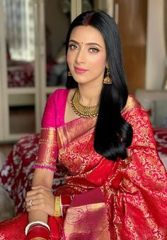 a woman in a red and gold sari sitting on a couch with her hand on her hip