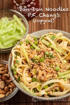 a bowl filled with noodles and vegetables on top of a wooden table next to nuts