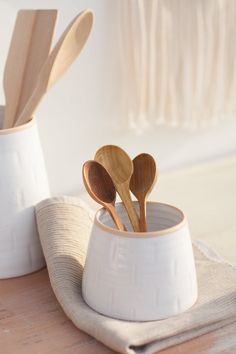 three wooden spoons are in a white cup on a table with a cloth napkin