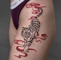 a woman's thigh with a tiger tattoo on the side and red flames coming out of it