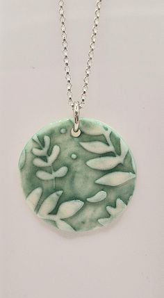 a green and white pendant with leaves on it