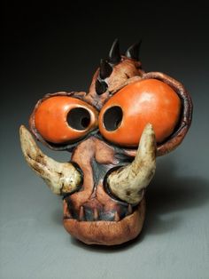 an orange and black mask with horns on it's head is sitting in front of a gray background