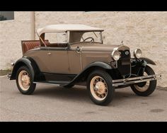 an old model car parked in front of a building