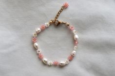 a pink and white beaded bracelet with gold clasps on a white cloth background